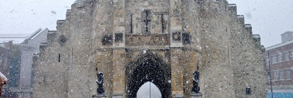 The Bargate in Southampton during heavy snowfall, with people walking and taking photos in front of the historic stone gate.