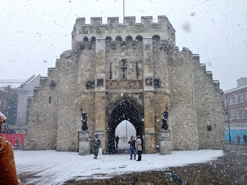 The Bargate in Southampton during heavy snowfall, with people walking and taking photos in front of the historic stone gate.